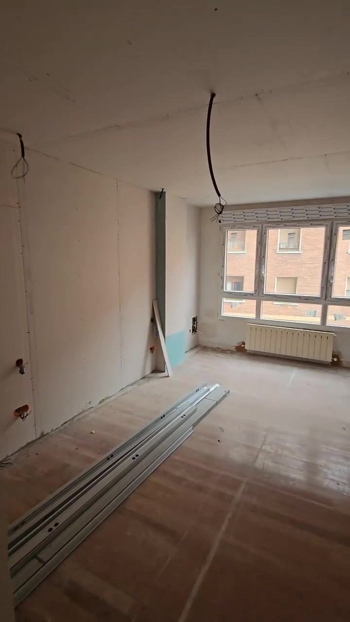 Fotograma del vídeo: estancia en obra con tabiquería de placa sin acabar, perfiles metálicos en el suelo y ventana al fondo.