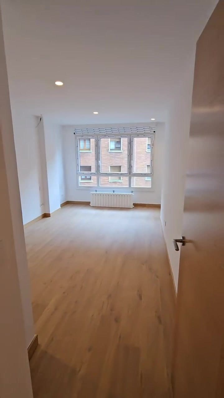 Habitación terminada tras una reforma de Ixaro: suelo de madera, paredes blancas y ventanal.